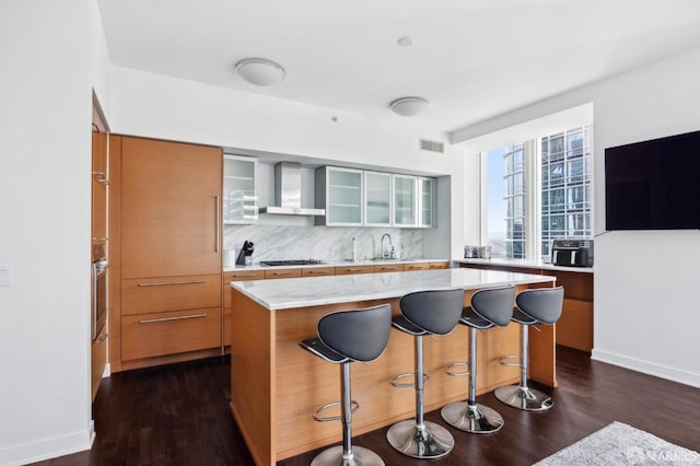 301 Mission St Unit 39A, San Francisco, CA 94105 - kitchen featuring wall chimney range hood, glass insert cabinets, dark wood finished floors, a breakfast bar, and a center island