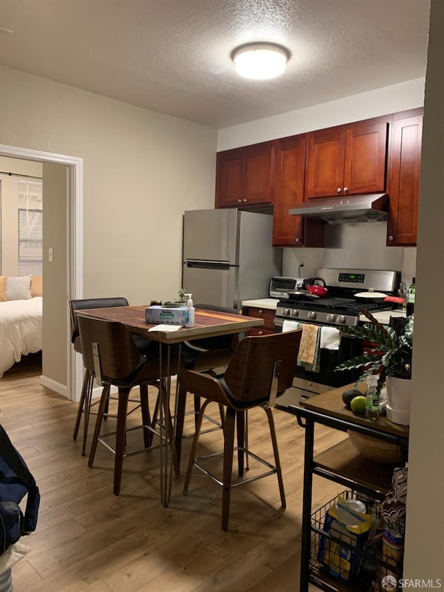 3-5 Sonoma St, San Francisco, CA 94133 - kitchen with under cabinet range hood, stainless steel appliances, a textured ceiling, and light wood-type flooring