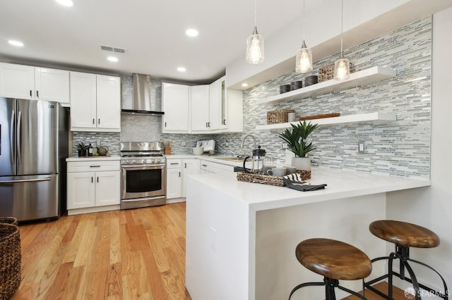 kitchen with stainless steel appliances, wall chimney exhaust hood, a peninsula, open shelves, and light countertops