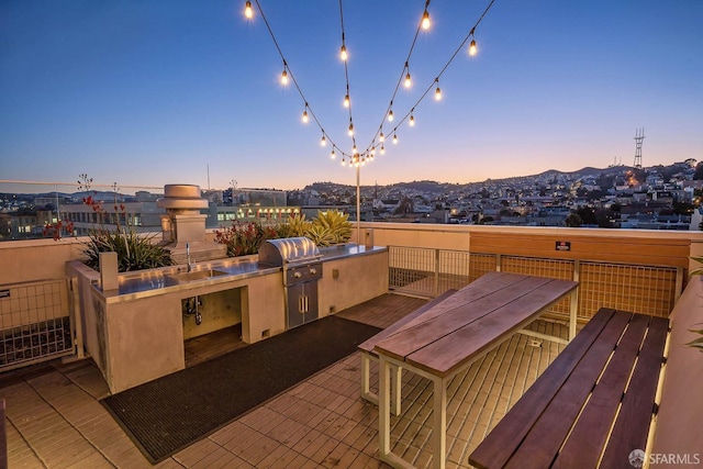 patio terrace at dusk with an outdoor kitchen, outdoor dining space, a sink, and grilling area