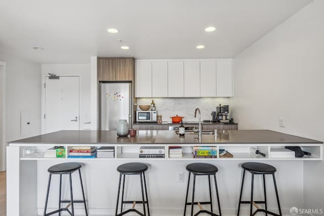 kitchen with a sink, stainless steel microwave, tasteful backsplash, refrigerator, and white cabinetry