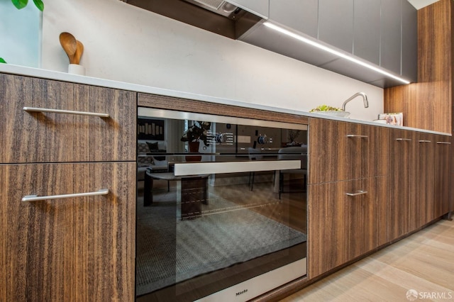 kitchen with wall oven, light wood-type flooring, light countertops, and modern cabinets