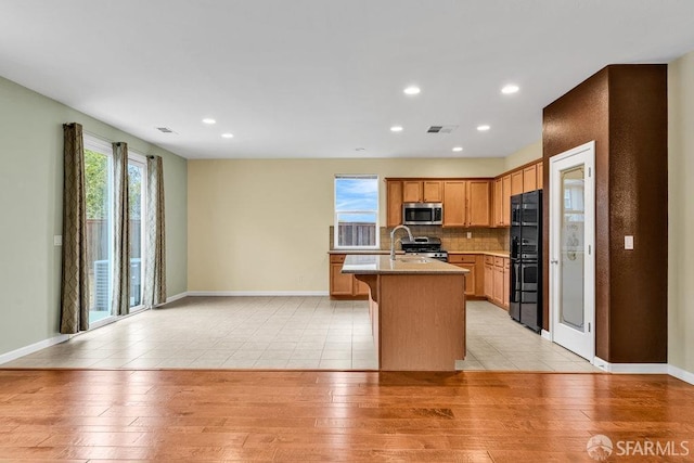 kitchen featuring appliances with stainless steel finishes, an island with sink, sink, backsplash, and light hardwood / wood-style floors