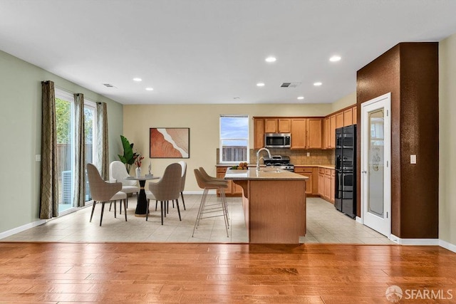 kitchen featuring appliances with stainless steel finishes, an island with sink, sink, decorative backsplash, and light hardwood / wood-style flooring