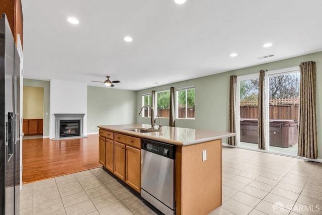 kitchen with sink, light tile patterned floors, an island with sink, stainless steel appliances, and light stone countertops