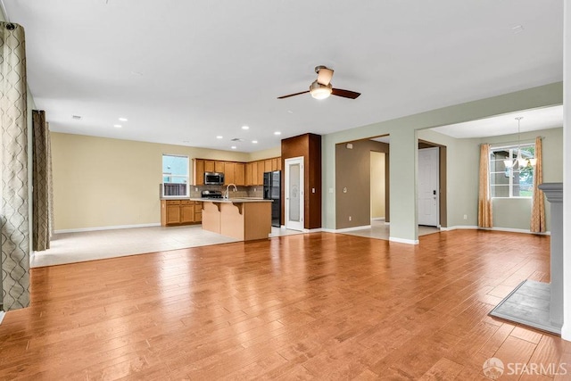 unfurnished living room featuring sink, ceiling fan with notable chandelier, plenty of natural light, and light hardwood / wood-style floors