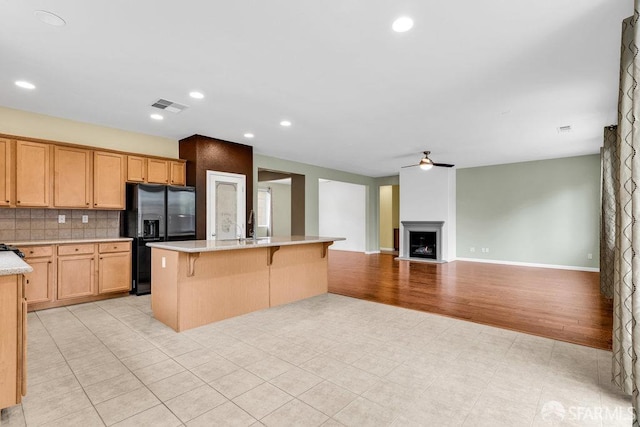 kitchen with a kitchen bar, black fridge with ice dispenser, tasteful backsplash, a center island with sink, and ceiling fan