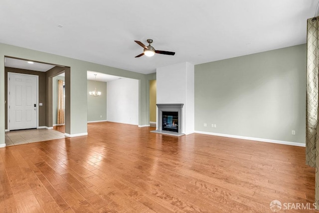 unfurnished living room with ceiling fan with notable chandelier and light hardwood / wood-style flooring