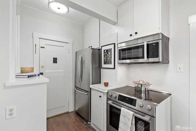 kitchen featuring white cabinets, light countertops, appliances with stainless steel finishes, ornamental molding, and dark wood-style floors