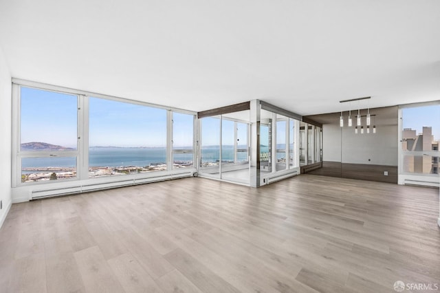 unfurnished living room with a wall of windows, a baseboard heating unit, a water view, light hardwood / wood-style floors, and a healthy amount of sunlight