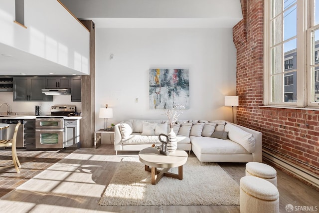 living room with a towering ceiling, brick wall, and light wood finished floors