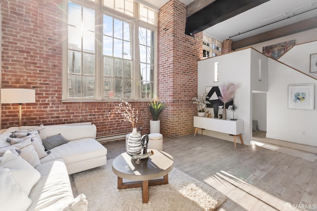 living room featuring brick wall, hardwood / wood-style floors, beamed ceiling, and a towering ceiling