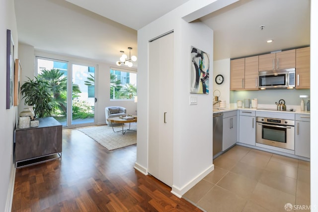 kitchen with stainless steel appliances, light countertops, a chandelier, baseboards, and dark wood finished floors