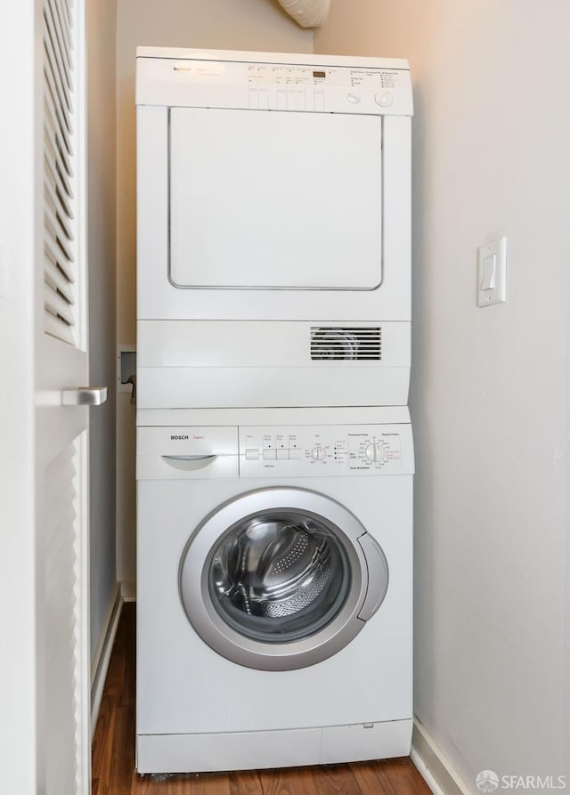 clothes washing area with stacked washer and clothes dryer, baseboards, and wood finished floors