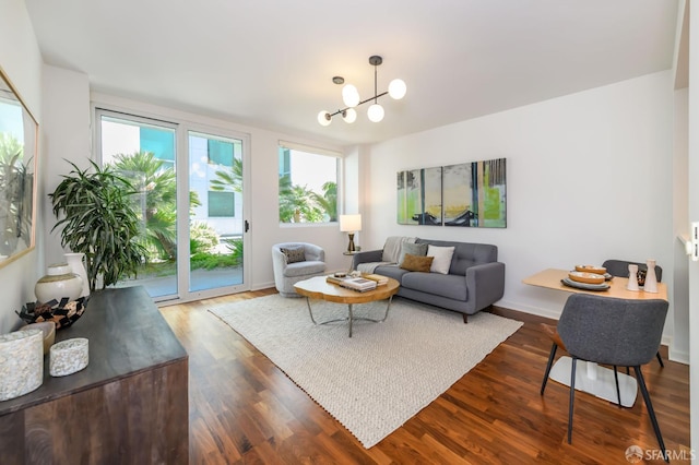 living room featuring dark wood-type flooring, a chandelier, and baseboards
