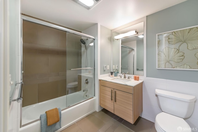 bathroom featuring toilet, shower / bath combination with glass door, vanity, tile patterned floors, and tile walls