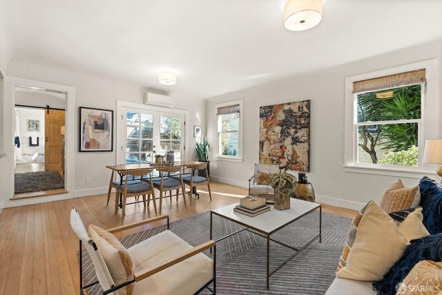 living room featuring a barn door, french doors, light hardwood / wood-style floors, and a wall mounted air conditioner