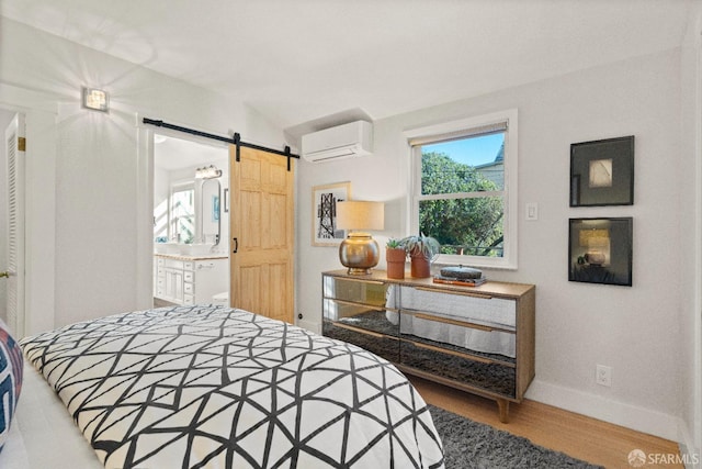 bedroom featuring an AC wall unit, a barn door, hardwood / wood-style floors, and ensuite bath