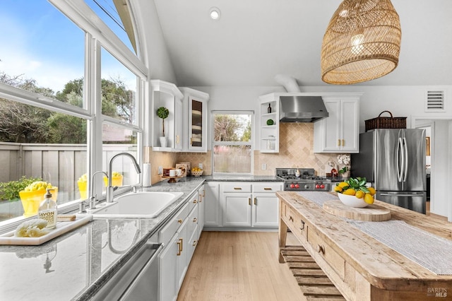 kitchen featuring wall chimney range hood, sink, hanging light fixtures, stainless steel appliances, and white cabinets