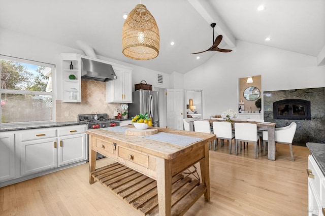 kitchen with tasteful backsplash, beamed ceiling, white cabinetry, stainless steel appliances, and wall chimney exhaust hood