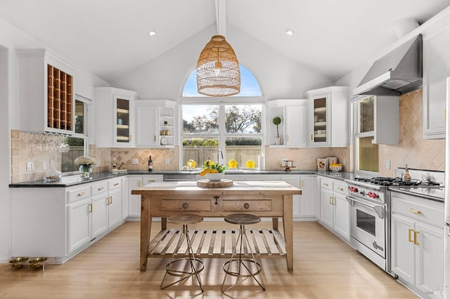 kitchen featuring wall chimney range hood, white cabinets, hanging light fixtures, and high end stove