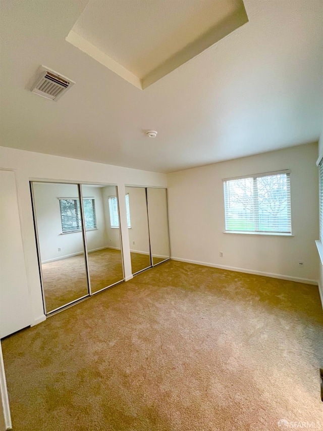 unfurnished bedroom with carpet, a raised ceiling, and two closets