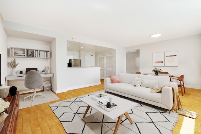 living room with baseboards, built in study area, and light wood-style floors