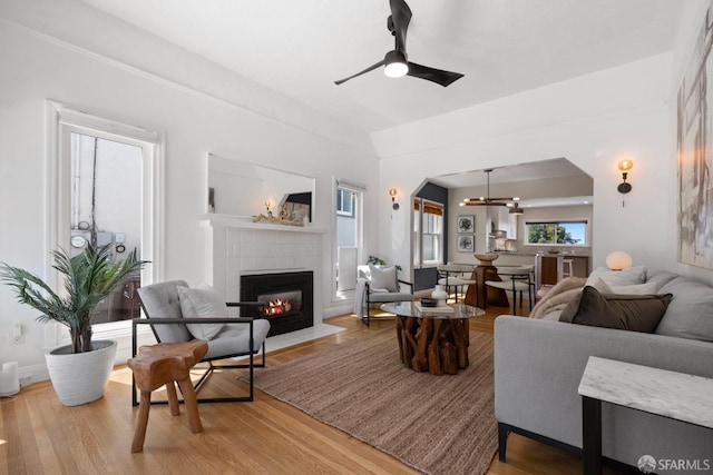 4551 Fairbairn Ave, Oakland, CA 94619 - living area featuring a tiled fireplace, light wood-style flooring, a ceiling fan, arched walkways, and a chandelier