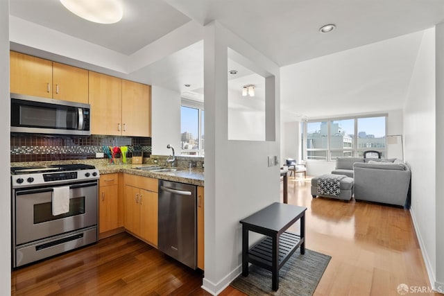 kitchen with light brown cabinetry, backsplash, stainless steel appliances, and a sink