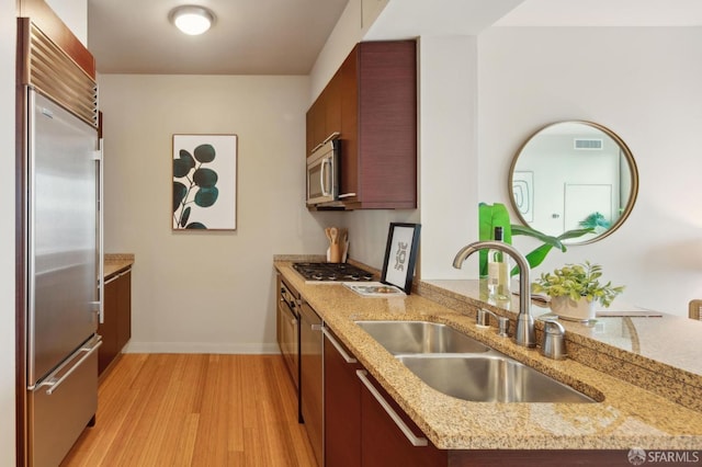 kitchen featuring light stone countertops, sink, stainless steel appliances, and light wood-type flooring