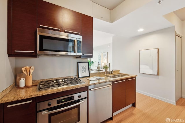 kitchen featuring appliances with stainless steel finishes, sink, light stone counters, and light hardwood / wood-style floors