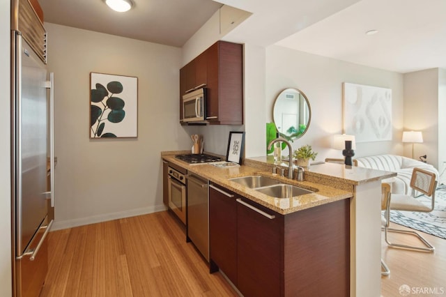 kitchen with light wood-type flooring, appliances with stainless steel finishes, kitchen peninsula, and sink