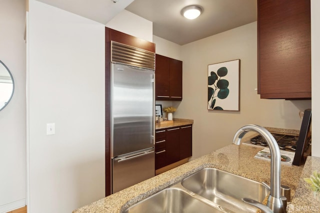 kitchen featuring built in refrigerator, sink, and light stone counters