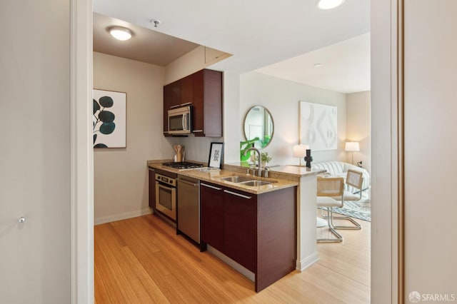 kitchen featuring light hardwood / wood-style floors, sink, dark brown cabinetry, stainless steel appliances, and light stone counters