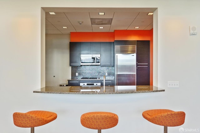 kitchen with kitchen peninsula, backsplash, stone counters, and stainless steel appliances