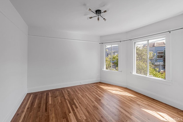 empty room with wood finished floors, baseboards, and a chandelier