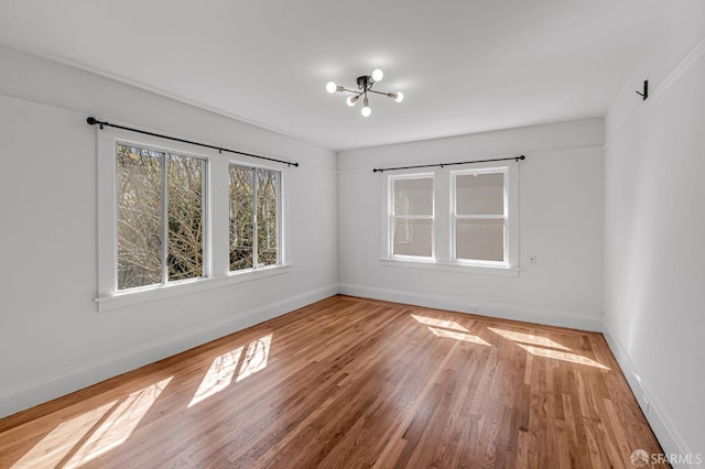 spare room featuring a notable chandelier, wood finished floors, and baseboards