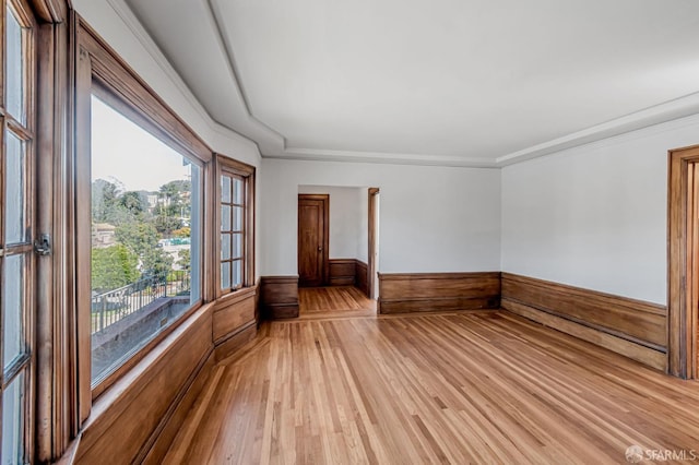 empty room featuring wooden walls, a wainscoted wall, light wood-style floors, and ornamental molding