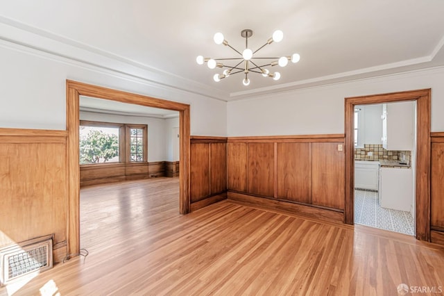 unfurnished dining area featuring visible vents, ornamental molding, an inviting chandelier, and a wainscoted wall