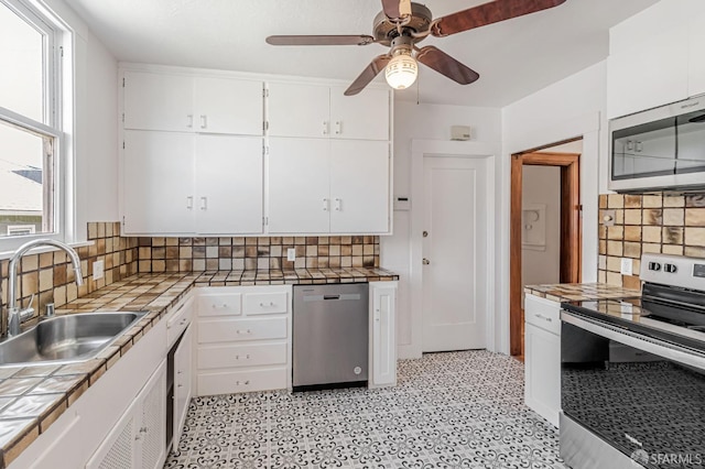 kitchen featuring a sink, appliances with stainless steel finishes, white cabinetry, and tile counters