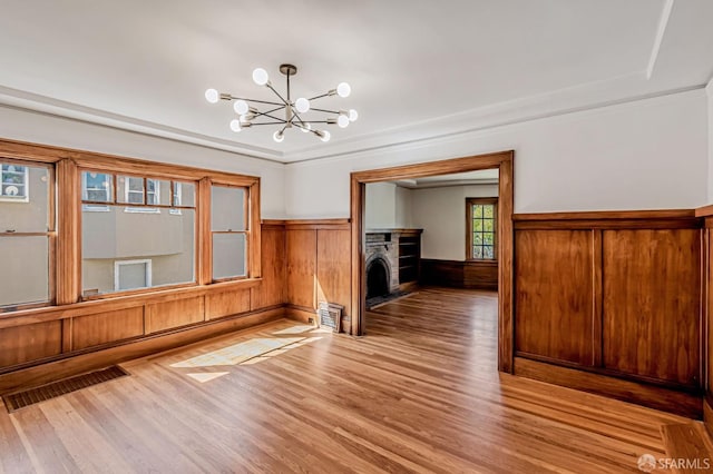 unfurnished living room featuring visible vents, a wainscoted wall, light wood-style flooring, a fireplace, and a chandelier