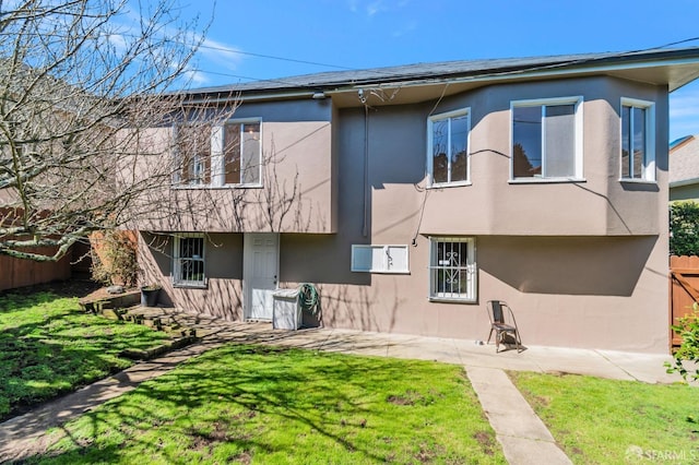 back of house featuring stucco siding, a lawn, and fence