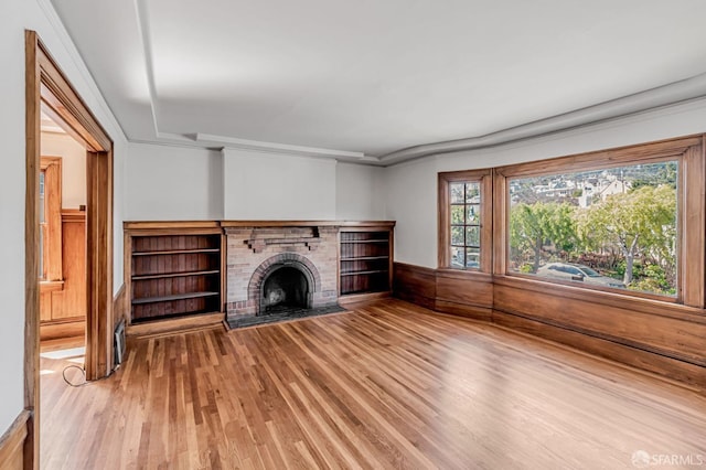 unfurnished living room featuring a fireplace, wood finished floors, and wainscoting