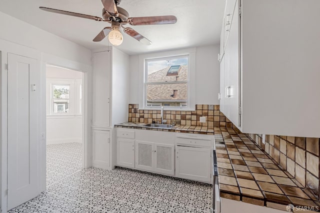 kitchen with backsplash, tile counters, white cabinets, a ceiling fan, and a sink