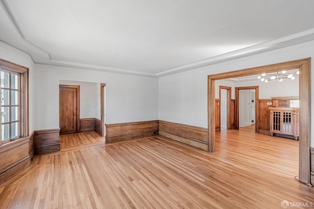 empty room with a notable chandelier, a wainscoted wall, light wood-style floors, and ornamental molding