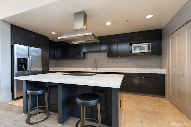 kitchen featuring a breakfast bar, stainless steel fridge, a kitchen island with sink, and range hood