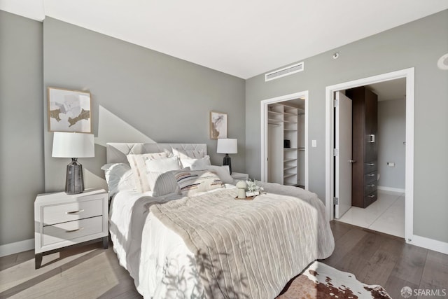 bedroom featuring a walk in closet, a closet, ensuite bath, and hardwood / wood-style flooring