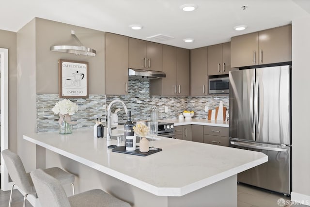 kitchen with kitchen peninsula, a kitchen bar, tasteful backsplash, stainless steel appliances, and sink