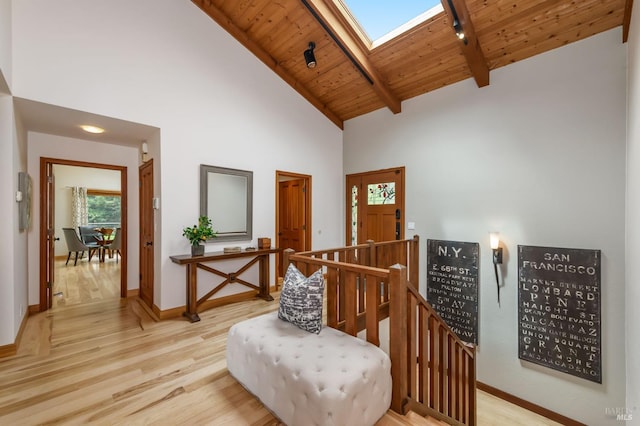interior space featuring high vaulted ceiling, light wood-style flooring, an upstairs landing, wooden ceiling, and a skylight