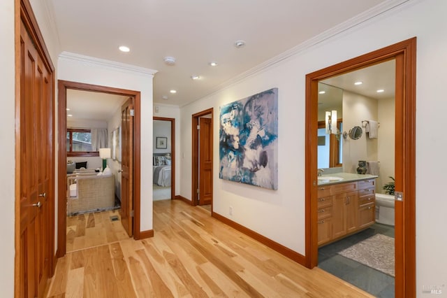 hall featuring a sink, light wood-style flooring, recessed lighting, baseboards, and ornamental molding